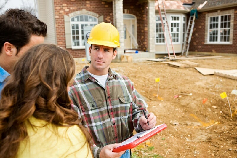 A contractor in a hard hat discusses a project with two homeowners.